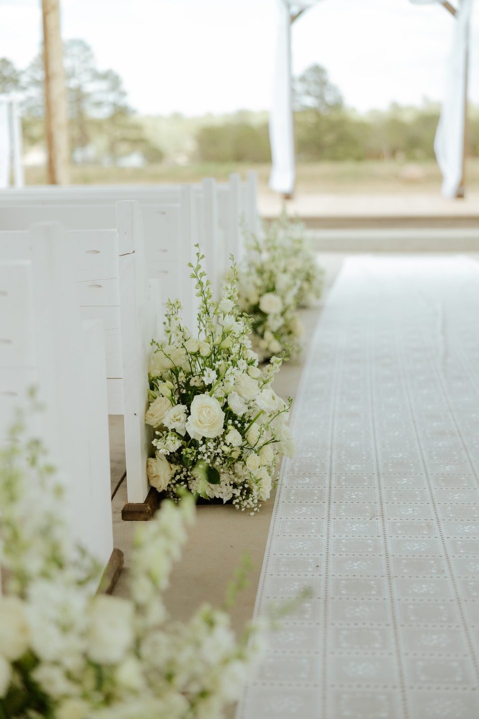 White wooden pew with cascading white floral arrangement along ceremony aisle